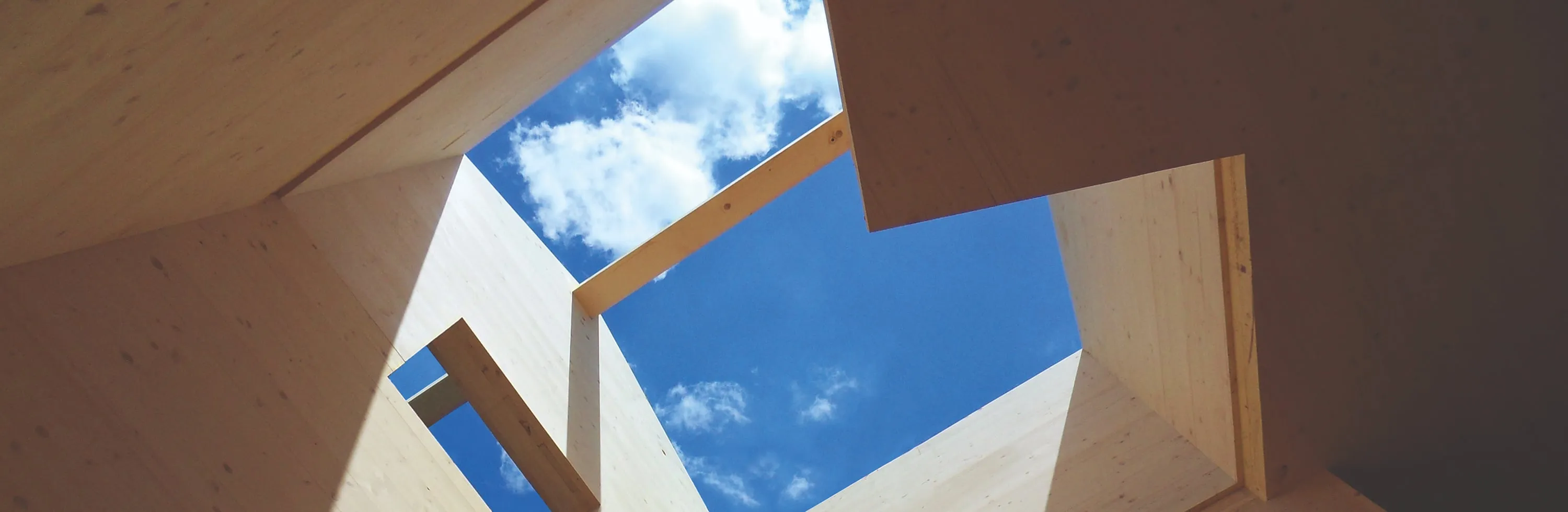 Estructura de madera laminada vista desde abajo, con el cielo al fondo